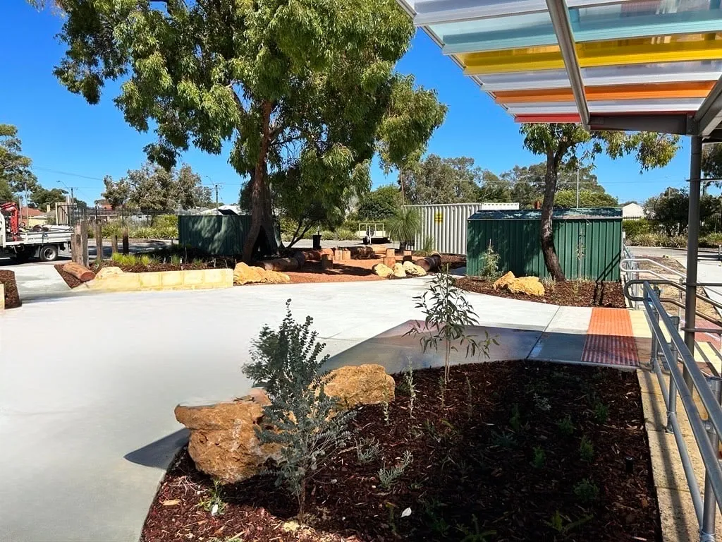 Broad grey concrete apron edged to limestone rocks and garden beds outside the Majella Primary School undercroft