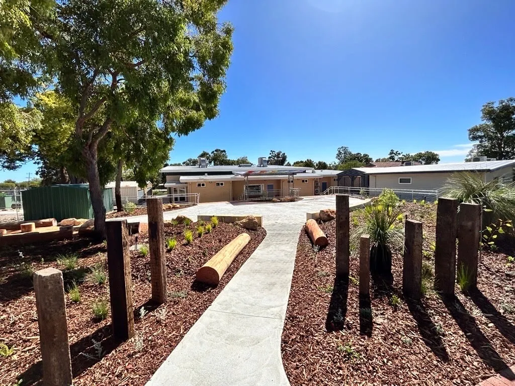 Grey concrete footpath winding between mulched native garden beds and timber bollards at Majella Primary School in Balga