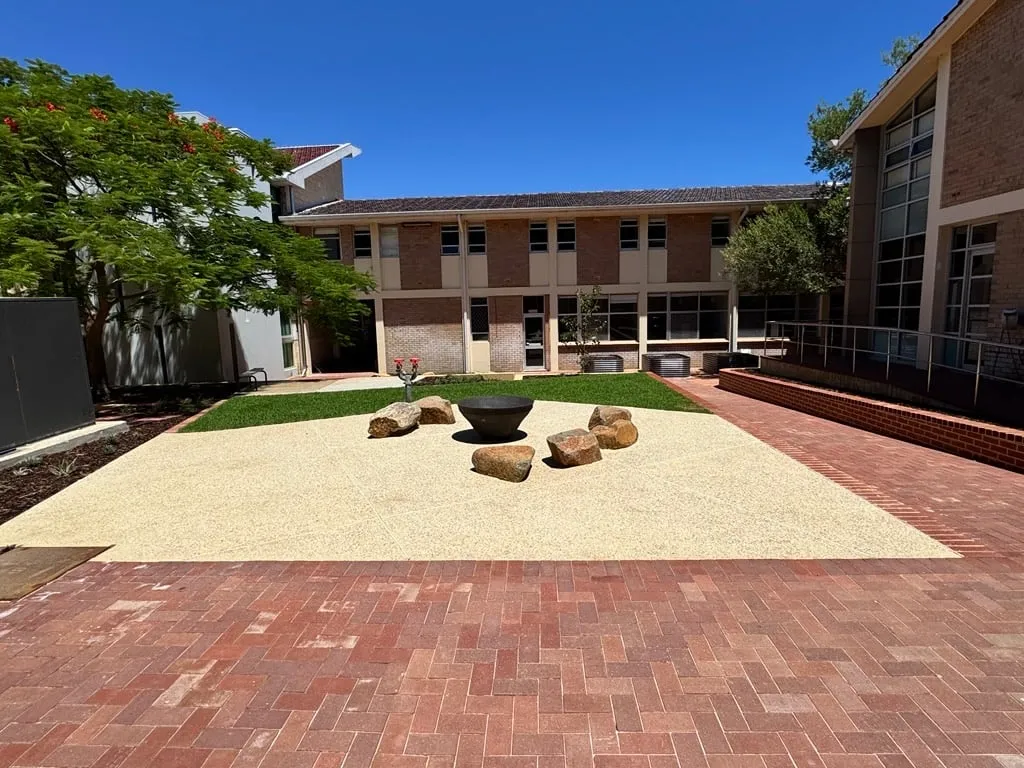 Pale exposed aggregate open space at PLC in Peppermint Grove, set square to a red brick surround with granite feature stones and a fire bowl