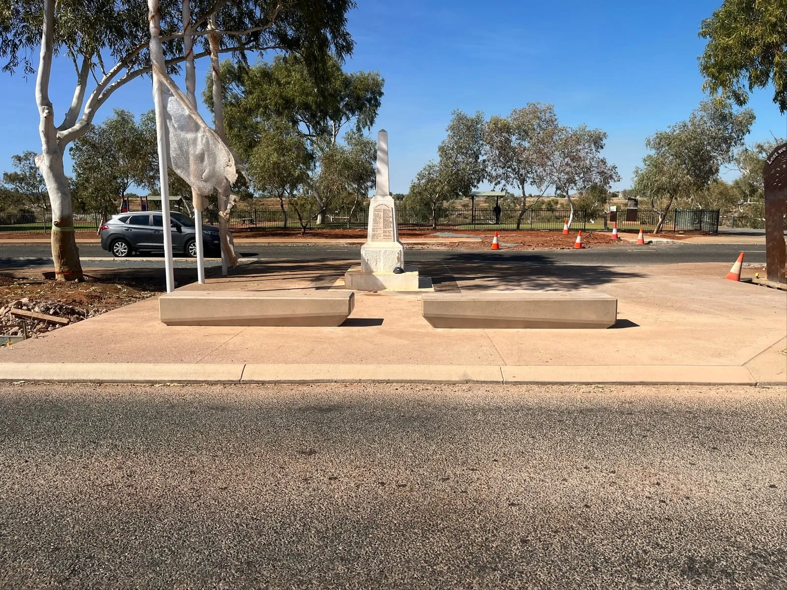 Two coloured concrete seating plinths either side of a war memorial obelisk on new coloured concrete paving