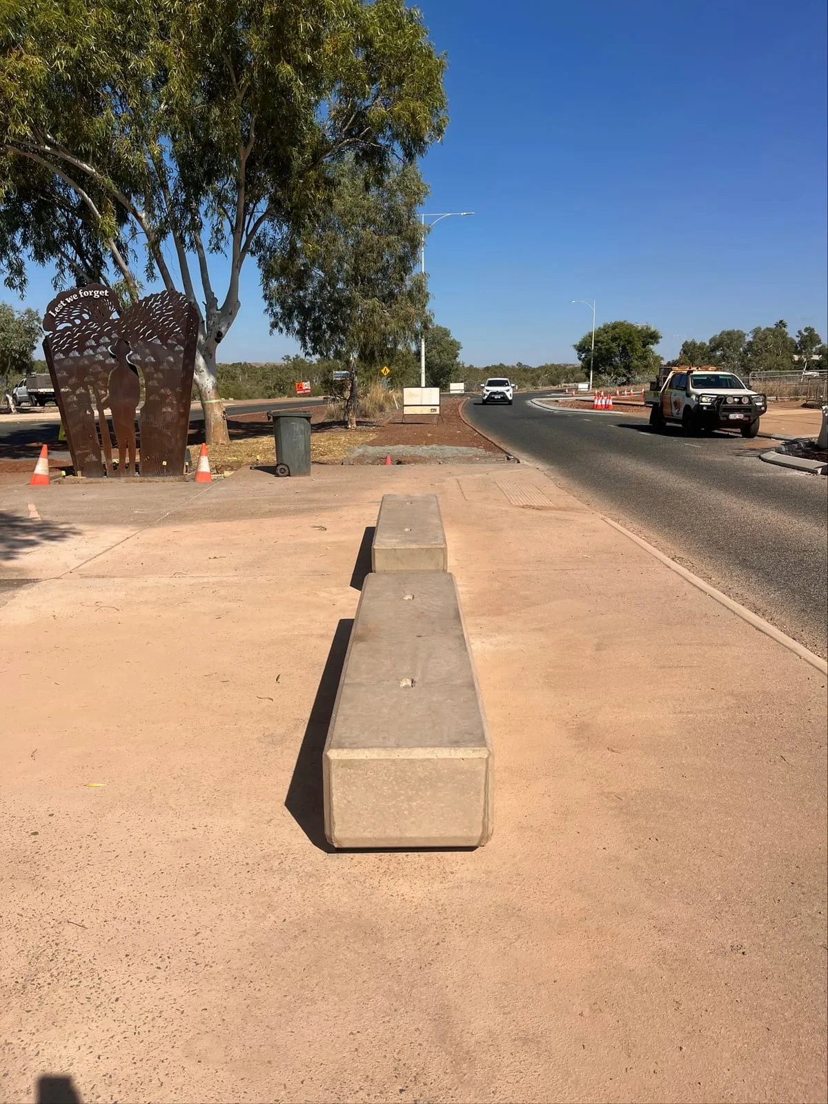 The finished plinths in line on the coloured concrete forecourt, with the memorial screen and the highway beyond