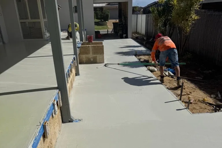 Screeding and finishing a freshly poured slab alongside a house, formwork still in place